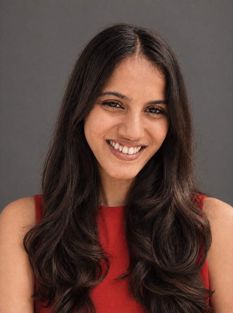 Aditi Vasa, smiling, in a red top against a grey background